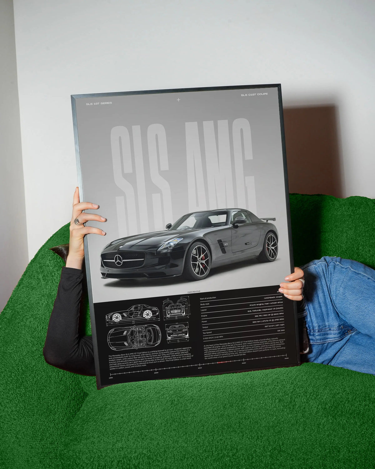 Person holding framed Mercedes-Benz SLS AMG GT poster while sitting on green sofa, premium supercar wall art with blueprint layout and technical specifications