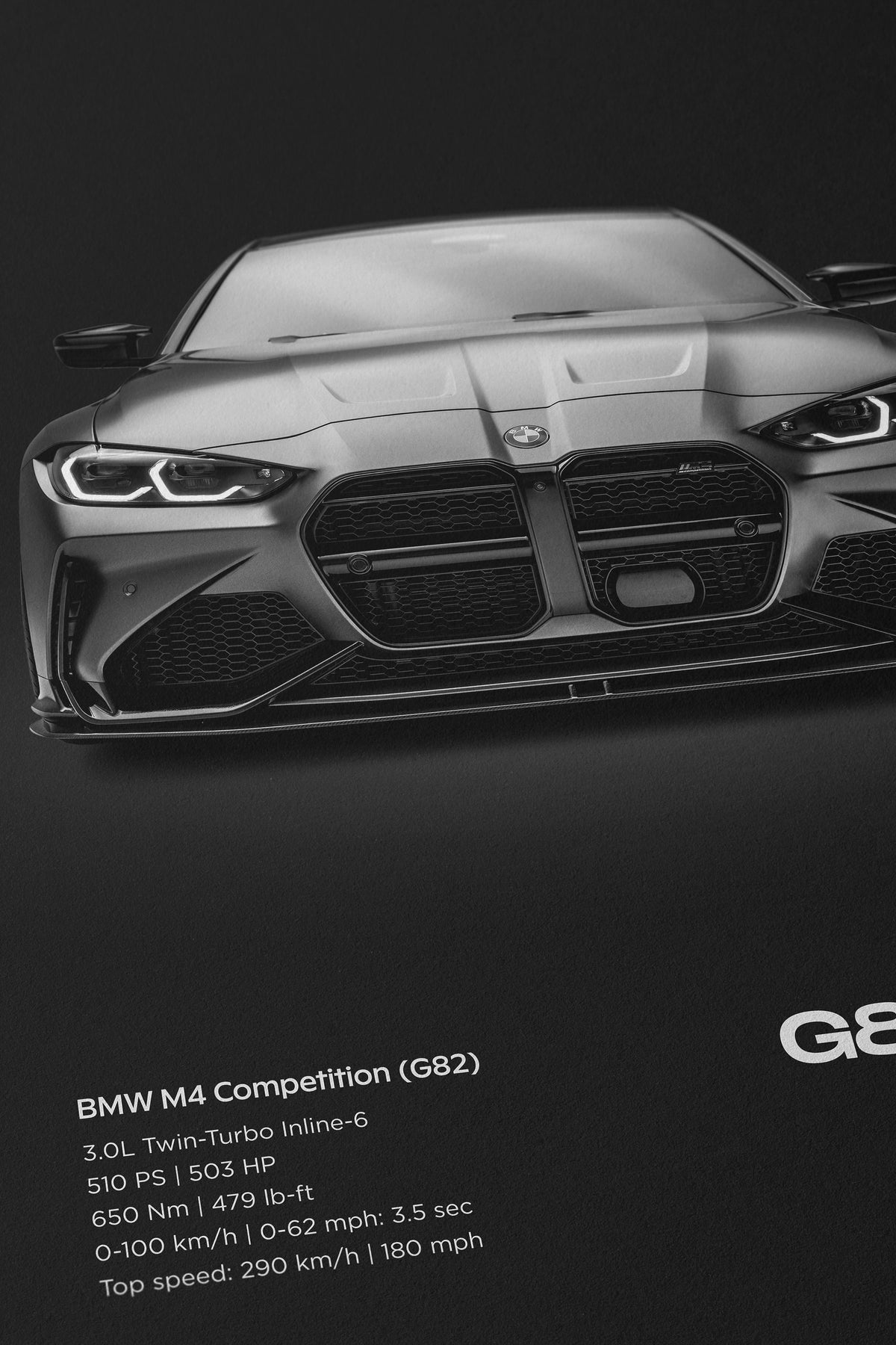 Close-up of black BMW M4 Competition G82 poster showing the front grille, headlights, and printed vehicle specifications on a dark background