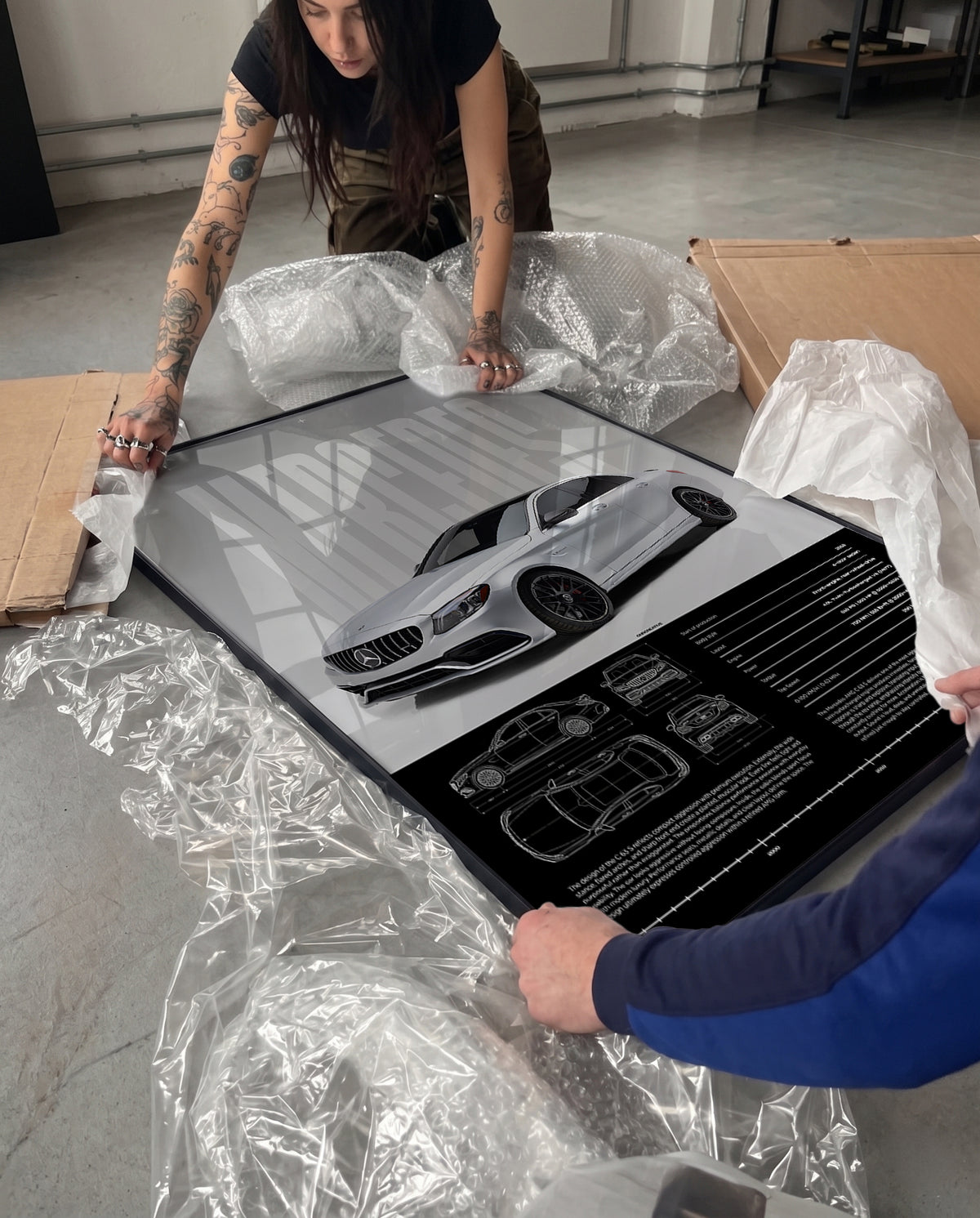 Unboxing a framed Mercedes-AMG C 63 S poster with protective packaging, bubble wrap, cardboard box, and black frame