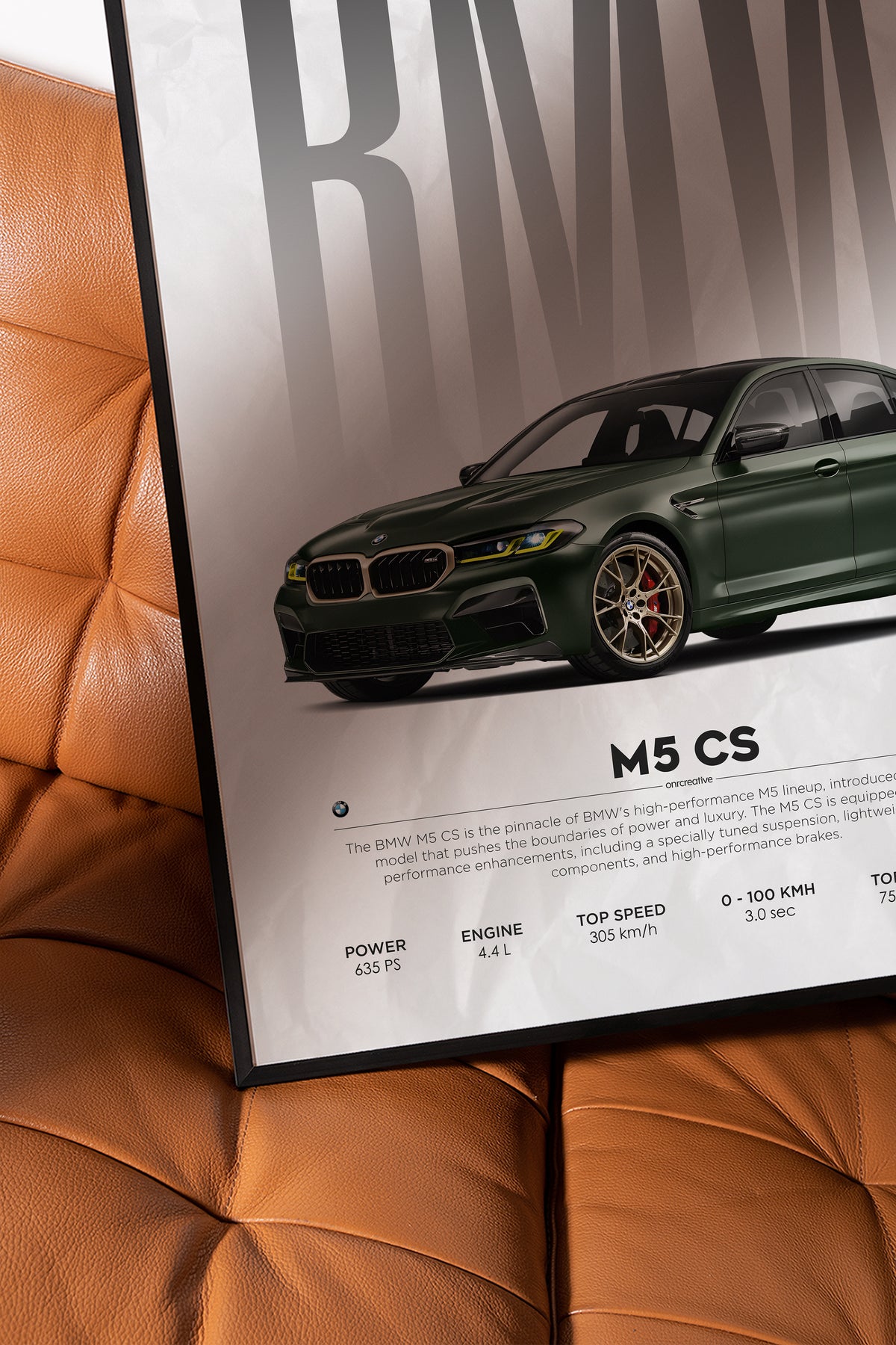Framed BMW M5 CS car poster leaning on a brown leather chair, showing a close-up of the green sedan artwork and performance specs