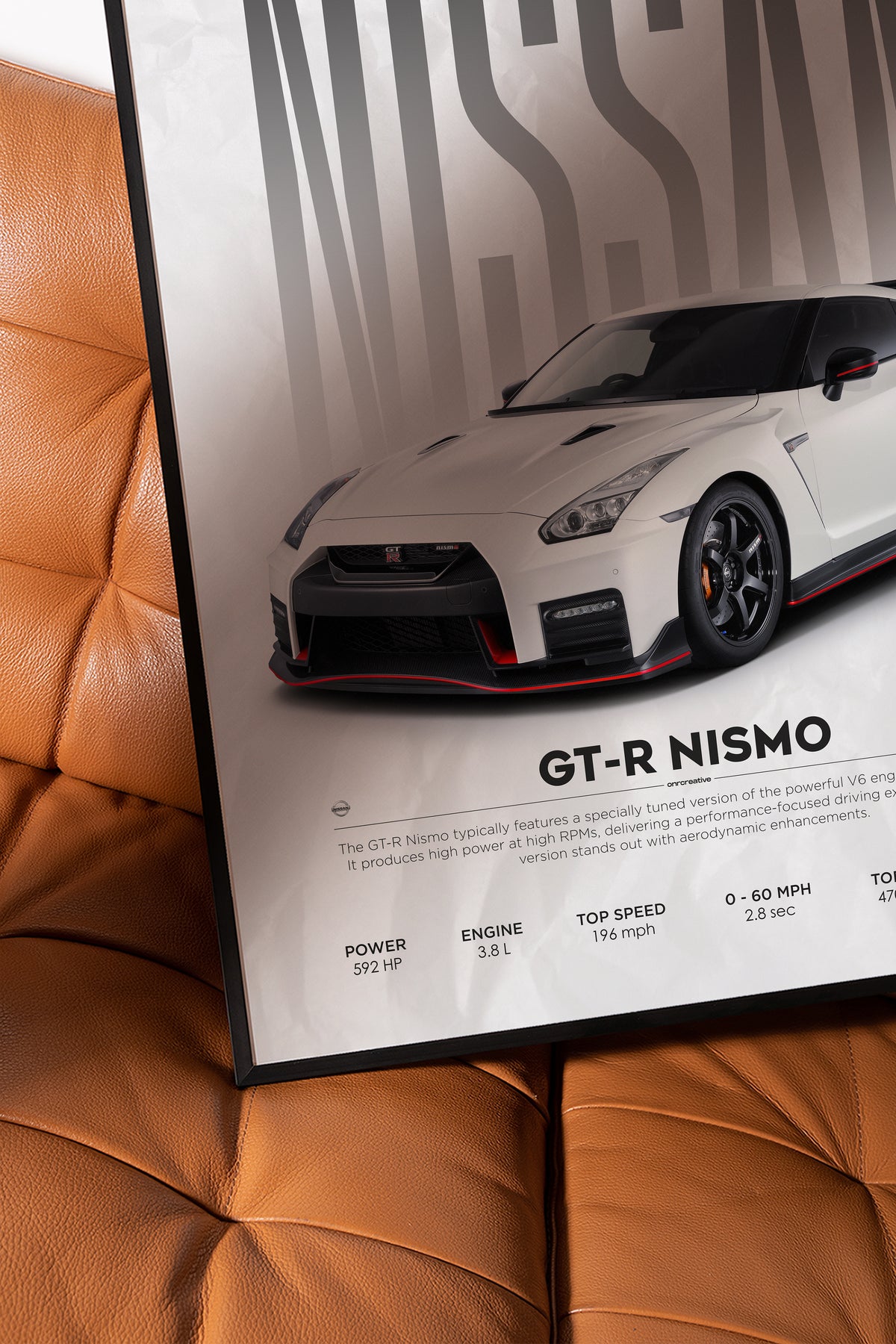 Framed Nissan GT-R Nismo poster resting on a brown leather chair, showing a close-up of the white sports car artwork and printed specs